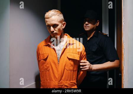 Agente di polizia che porta il sospetto nella sala interrogatori Foto Stock