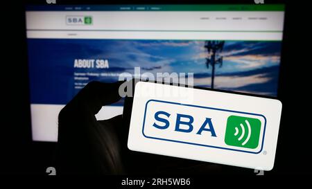 Persona che possiede uno smartphone con il logo della società statunitense SBA Communications Corporation sullo schermo di fronte al sito Web. Concentrarsi sul display del telefono. Foto Stock