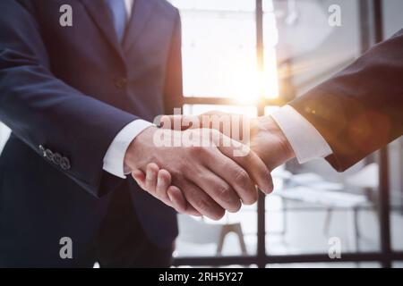 Uomini d'affari che scuotono le mani in piedi davanti alle finestre dell'ufficio Foto Stock