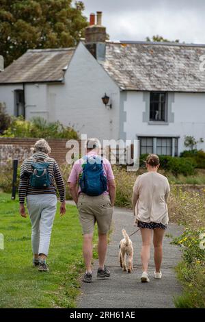 famiglia che cammina il cane in un villaggio lungo un sentiero. madre, padre e figlia che portano il cane per una passeggiata in campagna. Foto Stock