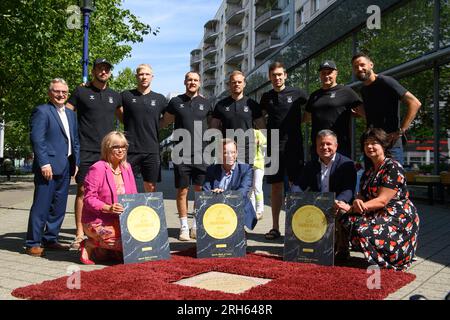 14 agosto 2023, Sassonia-Anhalt, Magdeburgo: Klaus Zimmermann (prima fila, l-r), Sottosegretario di Stato del Ministero degli interni e dello Sport della Sassonia-Anhalt, Lucas Meister, Magnus Saugstrup, Christian o'Sullivan, Omar Ingi Magnusson, Nikola Portner e gli allenatori Antoni Parecki e Bennet Wiegert stanno insieme a Siome Borris (ultima fila, l-r), sindaco della città di Magdeburgo, Steffen Schüller, presidente del Consiglio di amministrazione della City Marketing Association, sponsor Mario Spaniel e Regina-Dolores Stieler-Hinz, sindaco di Magdeburgo, dietro una targa di bronzo in granito che riporta la scritta "EHF Champions League" a Foto Stock