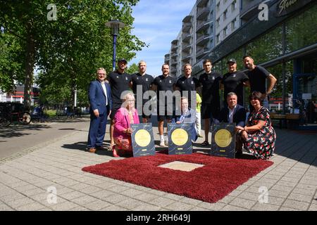 14 agosto 2023, Sassonia-Anhalt, Magdeburgo: Klaus Zimmermann (prima fila, l-r), Sottosegretario di Stato del Ministero degli interni e dello Sport della Sassonia-Anhalt, Lucas Meister, Magnus Saugstrup, Christian o'Sullivan, Omar Ingi Magnusson, Nikola Portner e gli allenatori Antoni Parecki e Bennet Wiegert stanno insieme a Siome Borris (ultima fila, l-r), sindaco della città di Magdeburgo, Steffen Schüller, presidente del Consiglio di amministrazione della City Marketing Association, sponsor Mario Spaniel e Regina-Dolores Stieler-Hinz, sindaco di Magdeburgo, dietro una targa di bronzo in granito che riporta la scritta "EHF Champions League" a Foto Stock