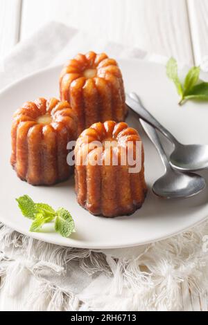 Caneles de bordeaux dessert dolce francese tradizionale da vicino in un piatto sul tavolo. Verticale Foto Stock