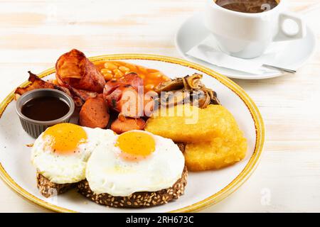 Uova fritte con salsicce, pepite, funghi e tazza di caffè. Βreakfast concetto. Foto Stock