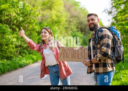 Felice coppia hitchhiking sulla strada cercando di fermare l'auto. Sono in cartoncino con iscrizione. Foto Stock