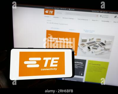 Persona che possiede un telefono cellulare con il logo dell'azienda svizzera te Connectivity Ltd. Sullo schermo davanti alla pagina Web aziendale. Concentrarsi sul display del telefono. Foto Stock