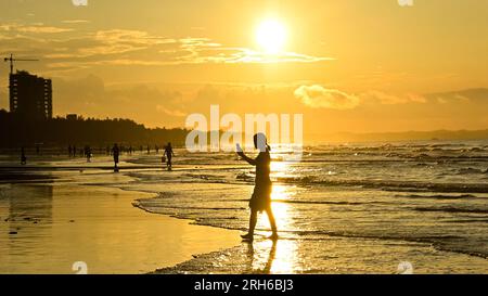 (230814) -- DONGXING, 14 agosto 2023 (Xinhua) -- i turisti si divertono all'alba sulla spiaggia di Jintan a Dongxing, nella regione autonoma di Guangxi Zhuang nel sud della Cina, 14 agosto 2023. La spiaggia di Jintan, situata nella parte meridionale dell'isola di Wanwei, ha una costa di 15 chilometri e prende il nome dal suo colore di sabbia dorata. (Xinhua/Zhang Ailin) Foto Stock