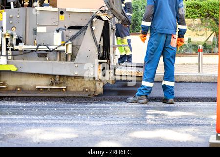 Frammento di applicazione di asfalto fresco nel lavoro di un'asfaltatrice su strada in un giorno d'estate. Foto Stock