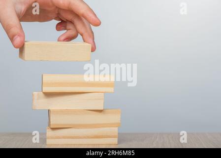 Rettangolo di legno in mano su sfondo grigio. Una mano mette un rettangolo di legno sopra gli altri per costruire un muro irregolare. Foto Stock