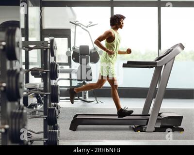 Foto a lunghezza intera di un ragazzo afroamericano che corre su un tapis roulant in palestra Foto Stock