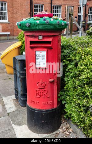 Classica cassetta per posta rossa decorata con un colorato cappello verde lavorato a maglia nel centro di Hythe nel Kent Foto Stock