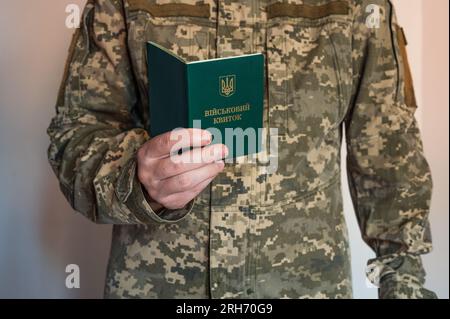 Soldato in tuta tattica tiene in mano un documento d'identità militare aperto. Uniforme pixel Ucraina Foto Stock