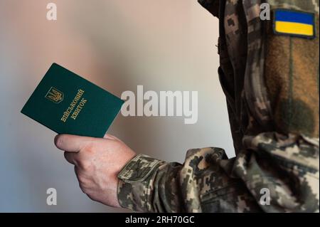 Soldato in costume da combattimento tattico tiene in mano un documento di identificazione militare. Uniforme pixel Ucraina Foto Stock