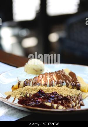 Pancake sottile con crema al cioccolato. Pancake con pasta al cioccolato, nocciole, salsa di ciliegia e una paletta di gelato su un piatto bianco su un piatto del ristorante Foto Stock
