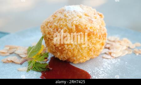 Gelato fritto con salsa di fragole, noci di mandorle e foglie di menta su piatto bianco. Foto Stock
