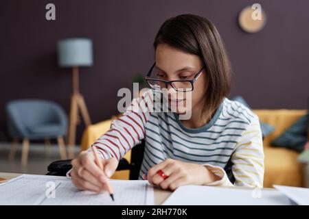 Ritratto di ragazza adolescente con disabilità indossare occhiali e fare test mentre studiano da casa, copia spazio Foto Stock