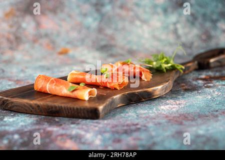Servizio di jamon in rotoli. Qualche pezzo di prosciutto a fette sottili su una tavola. Jamon e verdure. Vista frontale. Foto Stock