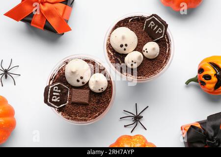 Composizione con delizioso tiramisù in tazze di plastica, confezione regalo e zucche per festeggiare Halloween su sfondo bianco, primo piano Foto Stock