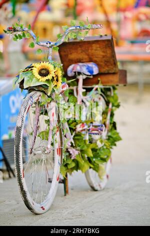 Bicicletta decorata con fiori e foglie multicolori in città. Oggetto artistico fatto a mano. Foto Stock