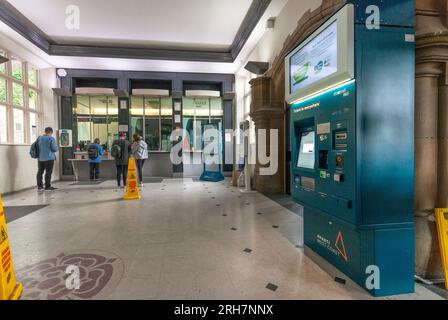 Biglietteria della stazione ferroviaria di Lancaster con un passeggero che acquista un biglietto, altri che fanno la fila e nessuno usa la biglietteria Foto Stock