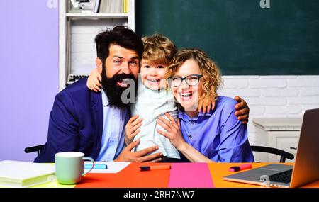 Torna a scuola. Carino bambino della scuola elementare con insegnanti in classe. Insegnanti felici, maschi e femmine, che si abbracciano con il piccolo scolaro. Felice Foto Stock