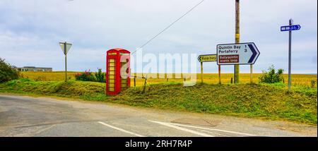 Lungo la Mourne Coastal Route, nella contea di Down, nell'Irlanda del Nord, una vecchia cabina telefonica rossa in disuso vicino alle indicazioni stradali per Kearney e Portaferry. Foto Stock