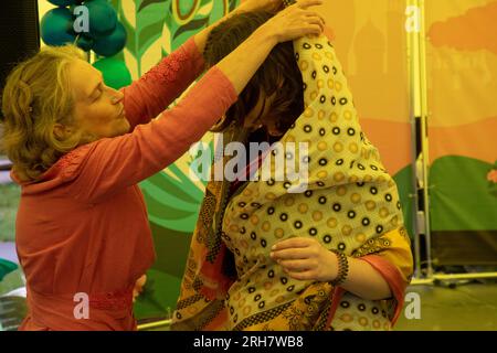 Mosca, Russia. 13 agosto 2023 Una donna insegna a un visitatore del Festival dell'India Day di indossare abiti indiani nazionali e sari al Parco dell'Isola dei sogni a Mosca, in Russia Foto Stock