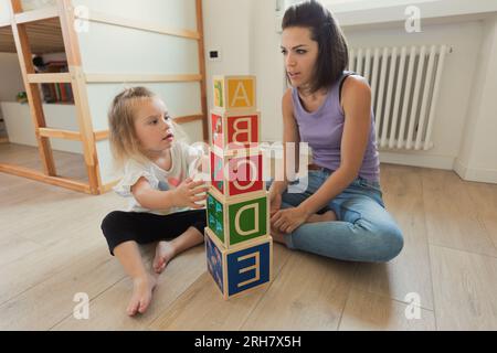 Giocando in camera da letto, la madre e la giovane figlia bionda si impegnano con i giocattoli di legno, imparando e godendosi il loro tempo di qualità insieme Foto Stock