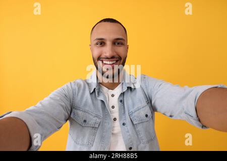 Giovane sorridente che scatta selfie su sfondo giallo Foto Stock