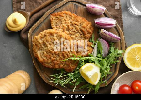 Deliziose schnitzels servite con limone, cipolla e microgreen su tavola grigia, piatti Foto Stock