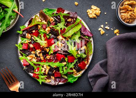 Insalata vegana con barbabietola, prugne secche, rucola, bietola svizzera e noci, fondo di pietra nera. Piatto vegetariano fresco e utile per un'alimentazione pulita Foto Stock