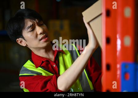 Lavoratore di sesso maschile che trasporta pesanti scatole di cartone, che soffre di mal di schiena. Concetto di lavoratori industriali e industriali Foto Stock