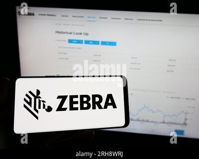 Persona che possiede un telefono cellulare con il logo della società americana Zebra Technologies Corporation sullo schermo davanti alla pagina Web. Concentrarsi sul display del telefono. Foto Stock