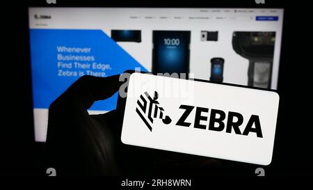 Persona che possiede uno smartphone con il logo della società statunitense Zebra Technologies Corporation sullo schermo di fronte al sito Web. Concentrarsi sul display del telefono. Foto Stock