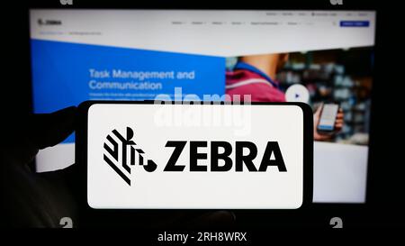 Persona che possiede il cellulare con il logo della società statunitense Zebra Technologies Corporation sullo schermo davanti alla pagina Web aziendale. Concentrarsi sul display del telefono. Foto Stock