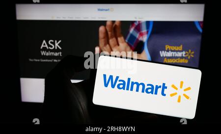 Persona che possiede uno smartphone con il logo della società di vendita al dettaglio statunitense Walmart Inc. Sullo schermo di fronte al sito Web. Concentrarsi sul display del telefono. Foto Stock