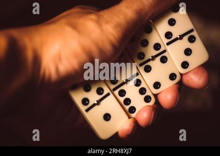 Primo piano delle piastrelle Domino in mano. Domino è uno dei giochi classici più famosi. Riprese in condizioni di scarsa illuminazione e profondità di campo ridotta. Foto Stock