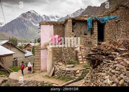 India, Ladakh, Valle di Suru, Panikhar, bambini che passano accanto a vecchie case di villaggio con il picco di Nun a 7235 metri di distanza Foto Stock