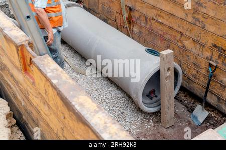 Costruttore installazione di un tubo di drenaggio in calcestruzzo di grande diametro protetto da un sistema di supporto per trincee durante lavori di drenaggio profondo Foto Stock