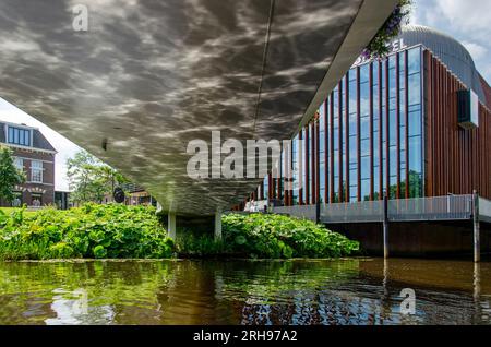 Zwolle, Paesi Bassi, 11 agosto 2023: Spettacolari riflessi d'acqua sotto il ponte pedonale Spinhuis con il teatro De Spiegel sullo sfondo Foto Stock