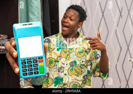 Foto di un uomo africano di colore che indossa un tessuto accanto a un armadio in tessuto mentre tiene e indica la macchina pos Foto Stock