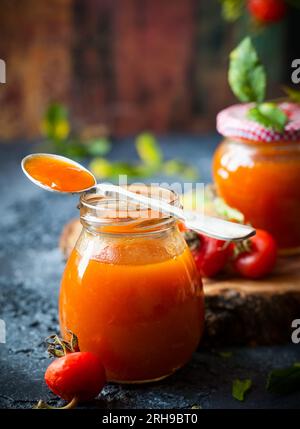 Marmellata di fianchi rosa in vaso con frutti di bosco freschi e foglie Foto Stock