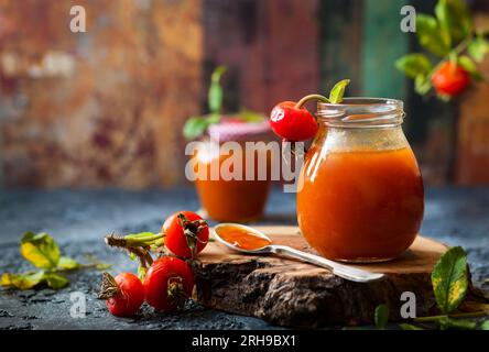 Marmellata di fianchi rosa in vaso con frutti di bosco freschi e foglie Foto Stock