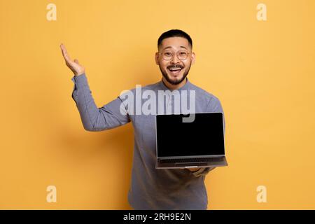Great Website. Excited Asian Man Holding Laptop Computer With Blank Screen Foto Stock