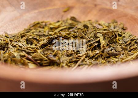 Foglie di tè essiccate dal sencha giapponese in una ciotola rustica di legno. Primo piano dell'ingrediente verde essiccato Foto Stock