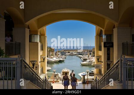 St Julians, Malta - 2 agosto 2023: Persone che camminano lungo i gradini dello sviluppo di Portomaso con barche e yacht nel porto turistico. Foto Stock