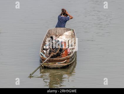 Una donna siede sulla prua di una barca e regola la sua acconciatura, Thailandia Foto Stock