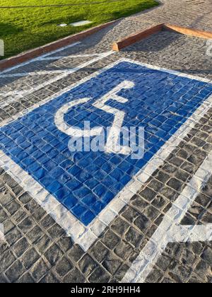 Parcheggio con cartello blu dipinto di sedia a rotelle su asfalto, posti auto per disabili Foto Stock