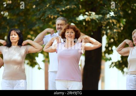 Gruppo di persone attive e anziane, uomini e donne che si allenano all'aperto nel parco, facendo esercizi di riscaldamento Foto Stock