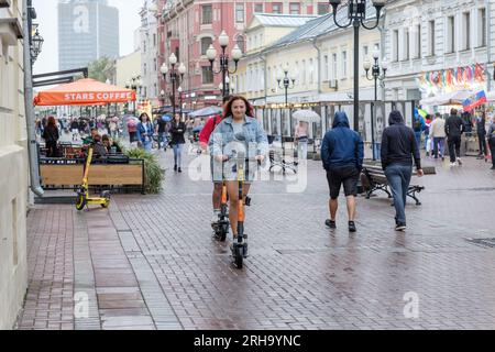Una ragazza guida uno scooter elettrico lungo una strada cittadina in un giorno di pioggia. Mosca. Russia. 13 agosto 2023. Foto Stock